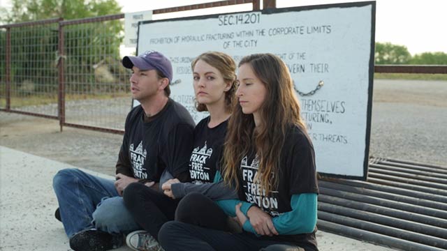 Adam Briggle, Tara Linn Hunter and Niki Chochrek sit at the entrance gate of a Vantage Energy gas well site on the edge of Denton, Texas' west side.